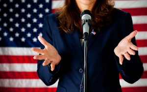 Woman politician standing at microphone with American flag in background